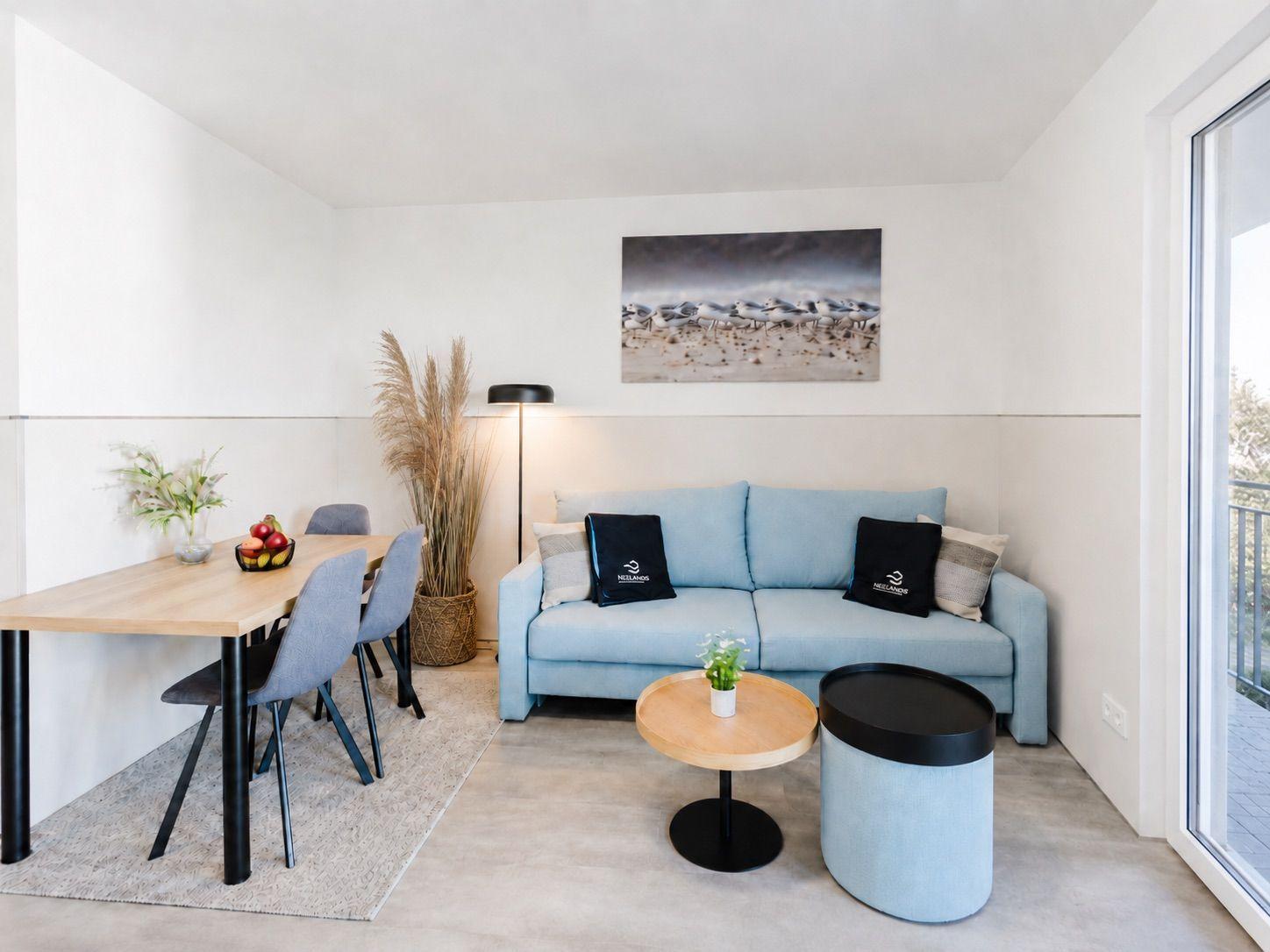 Wohn- und Essbereich mit Sofa, Tisch und Stühlen. Wandbild und Pflanzen sichtbar.