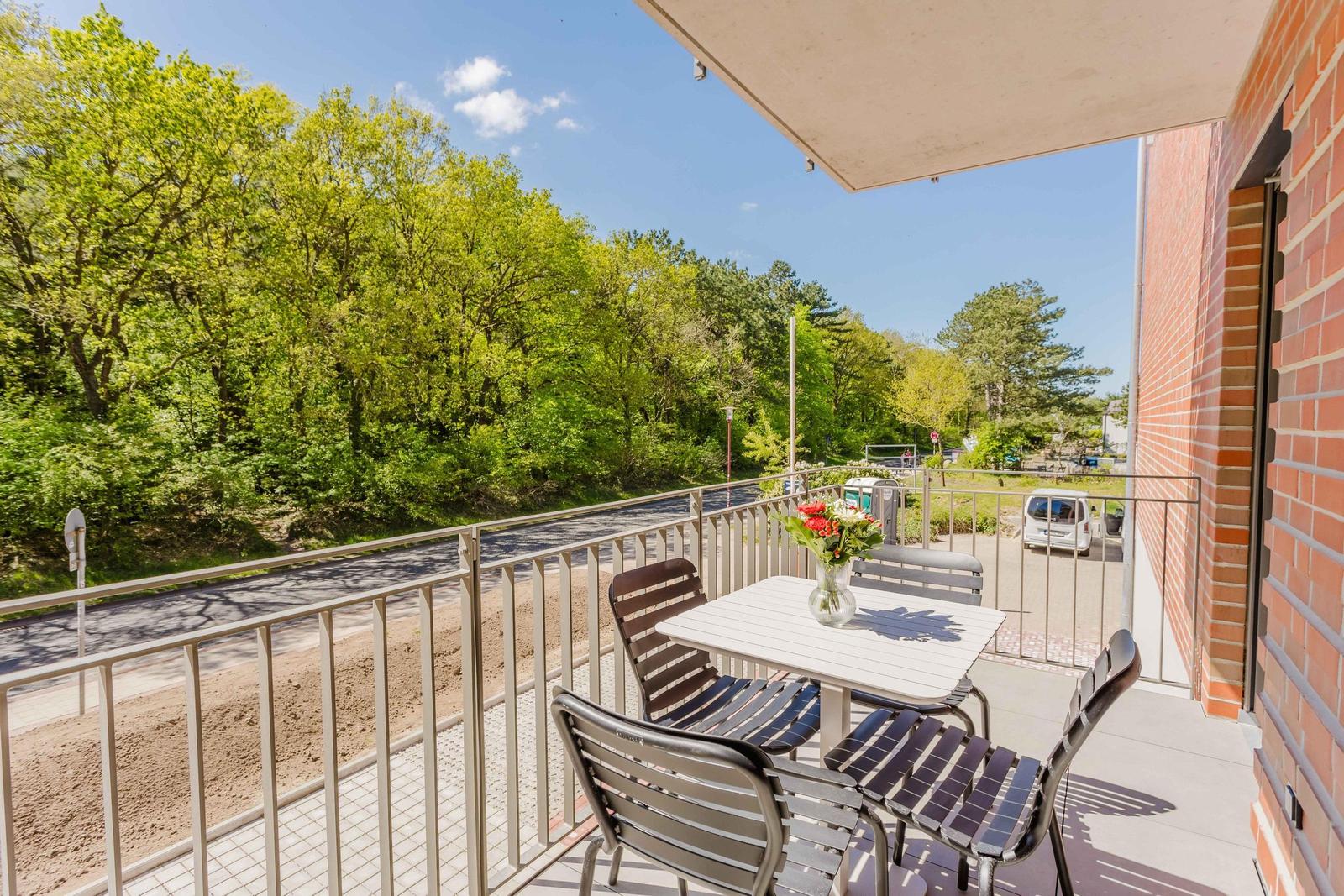 Terrasse mit Tisch und Stühlen, Blick auf grüne Bäume und Straße.