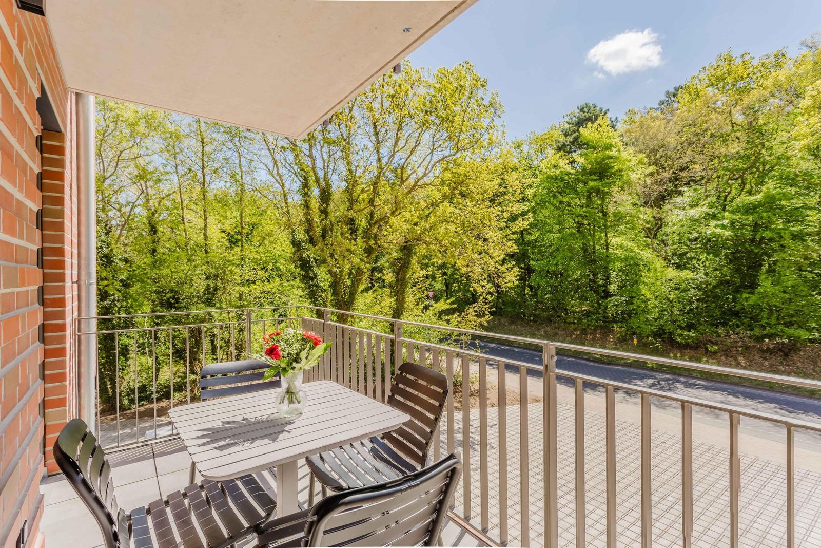 Terrasse mit Tisch und Stühlen, Blick auf grüne Bäume und Straße.