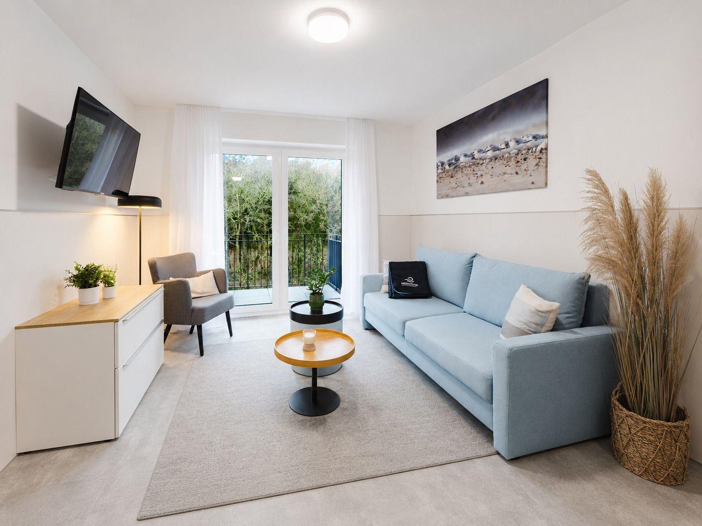 Wohnzimmer mit Sofa, Couchtisch und TV. Balkon mit Blick auf Grün.