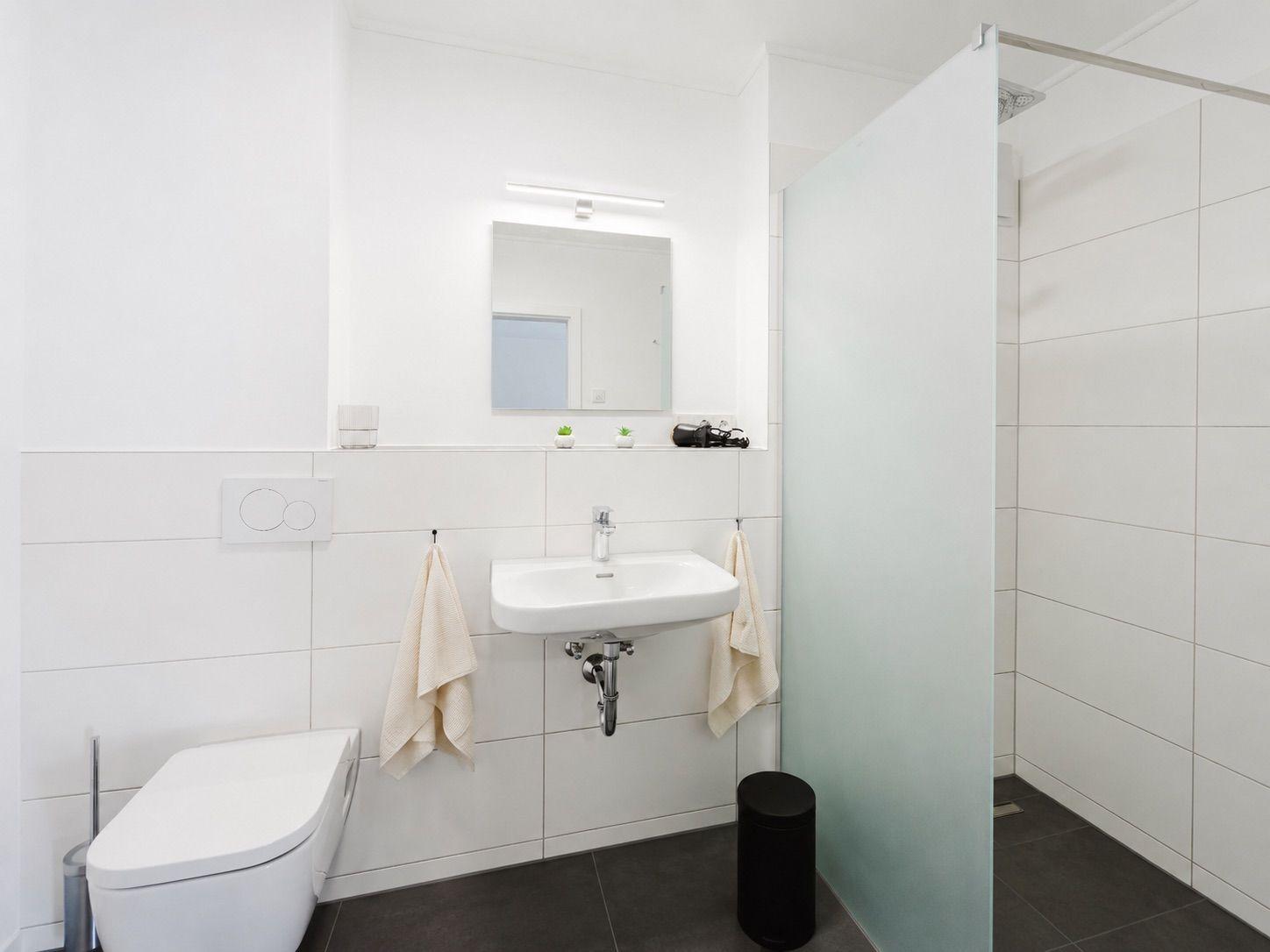 Bathroom with shower, sink, and toilet. White tiles and gray floor.