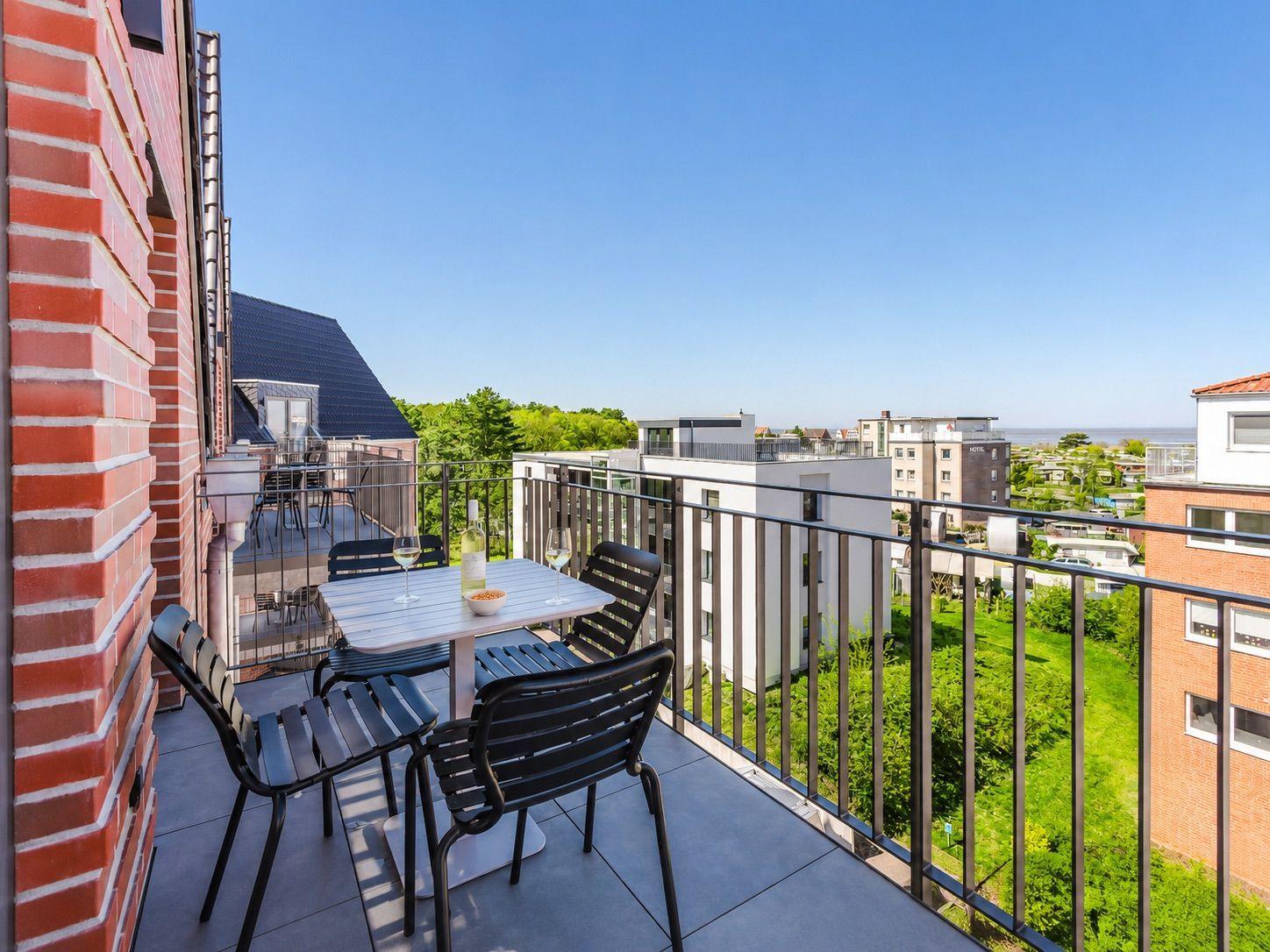 Terrace with table and chairs. View of residential buildings and green areas. Clear blue sky.