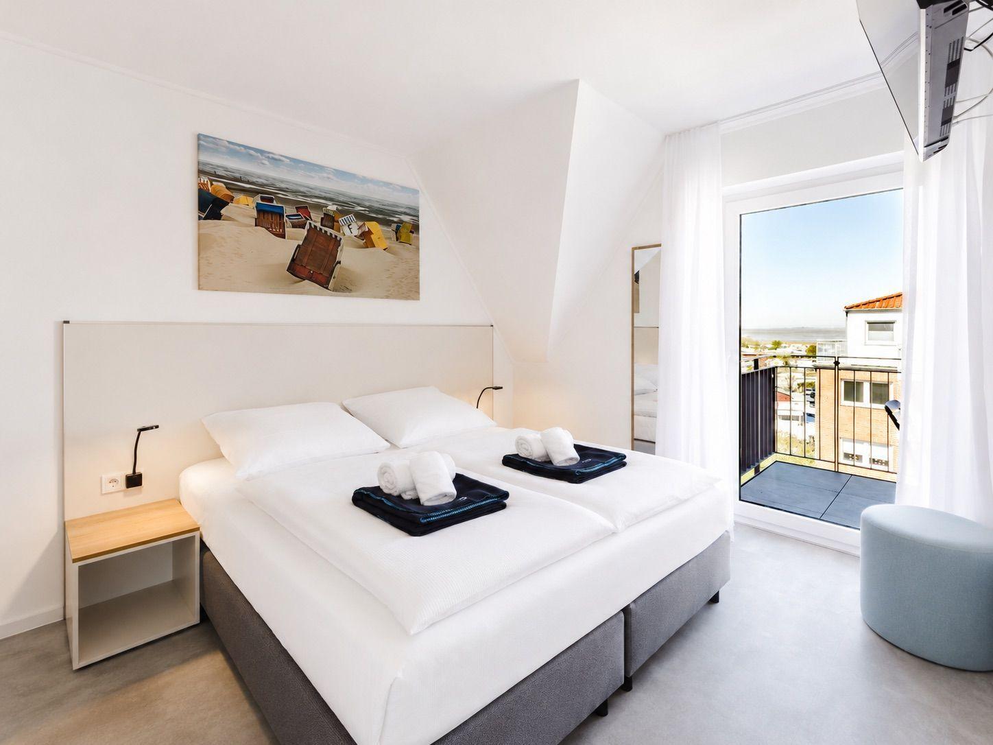 Bedroom with double bed, balcony, and wall art of beach chairs.