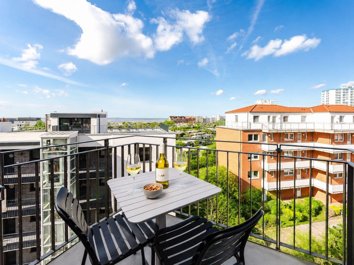 Terrasse mit Tisch, zwei Stühlen, Wein und Nüssen. Blick auf Gebäude und Grünflächen.