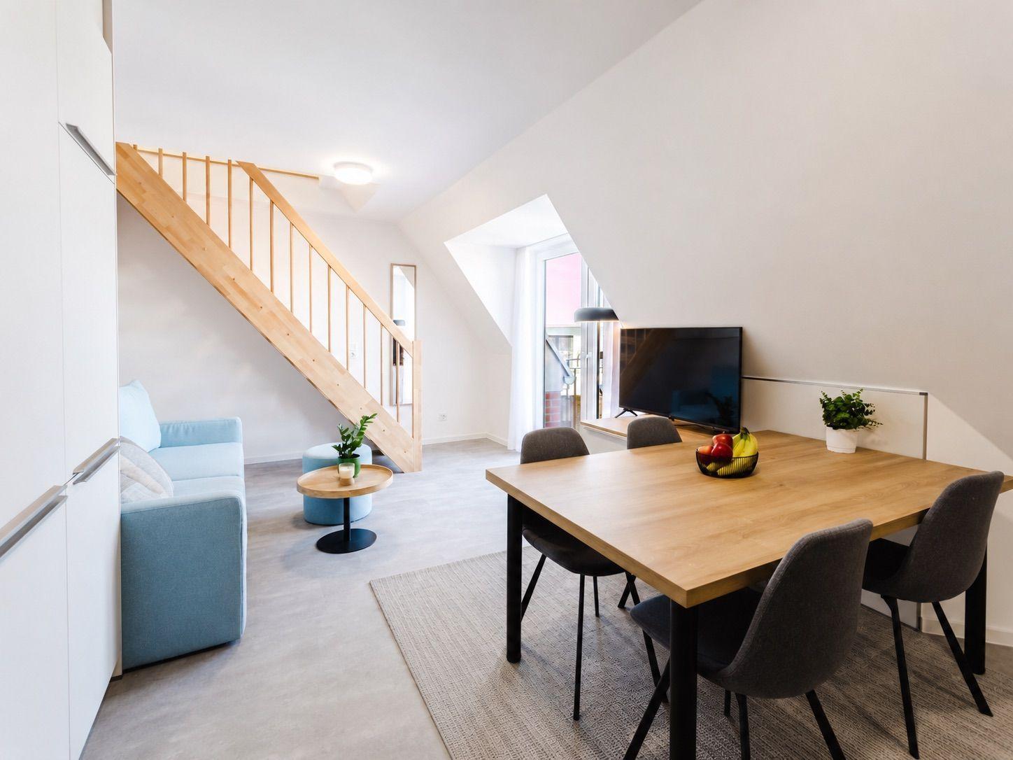 Wohn- und Essbereich mit Holztisch, Stühlen, Sofa und Holztreppe.