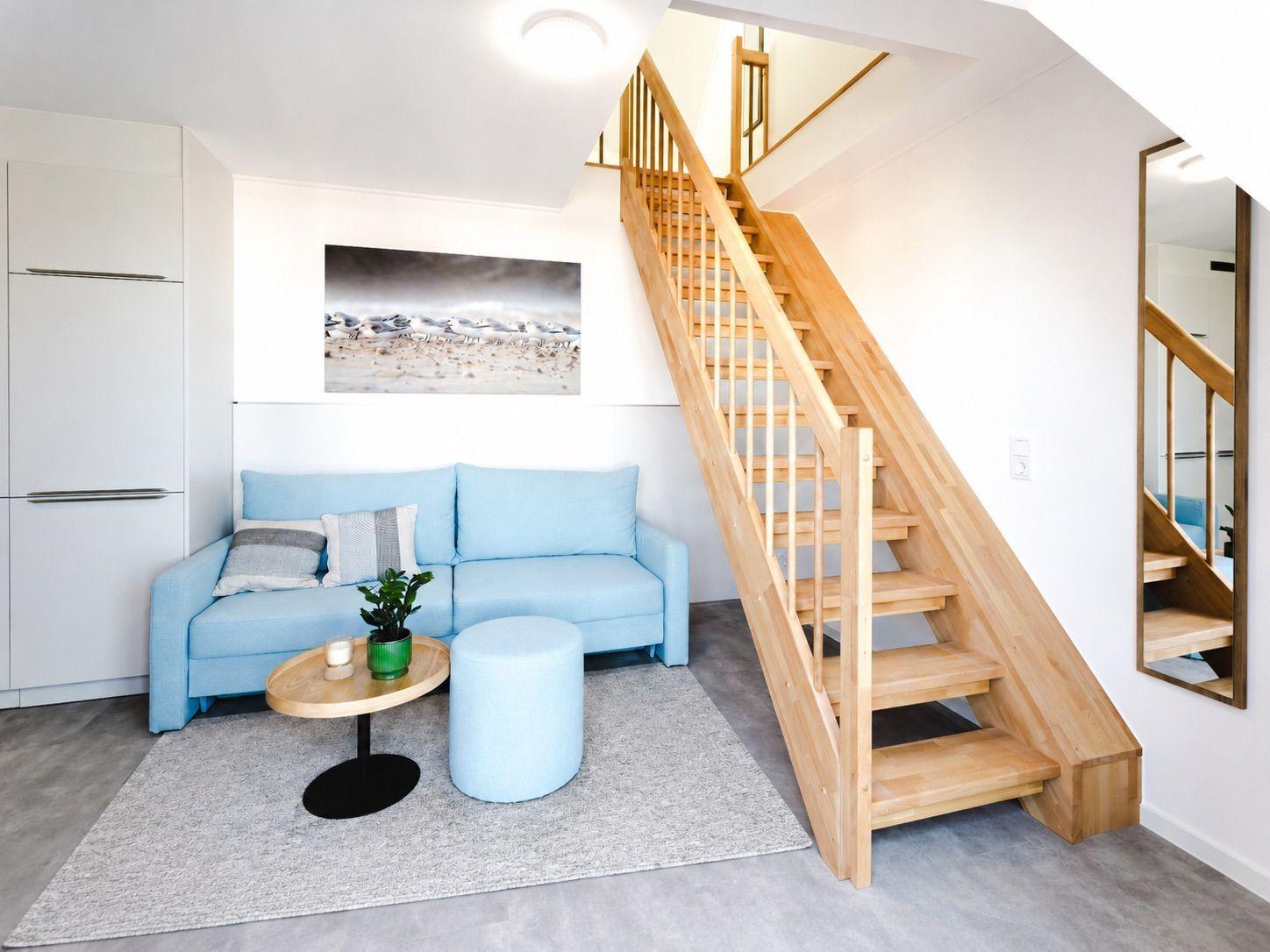 Wohnzimmer mit blauem Sofa, Holztreppe und Wandspiegel.