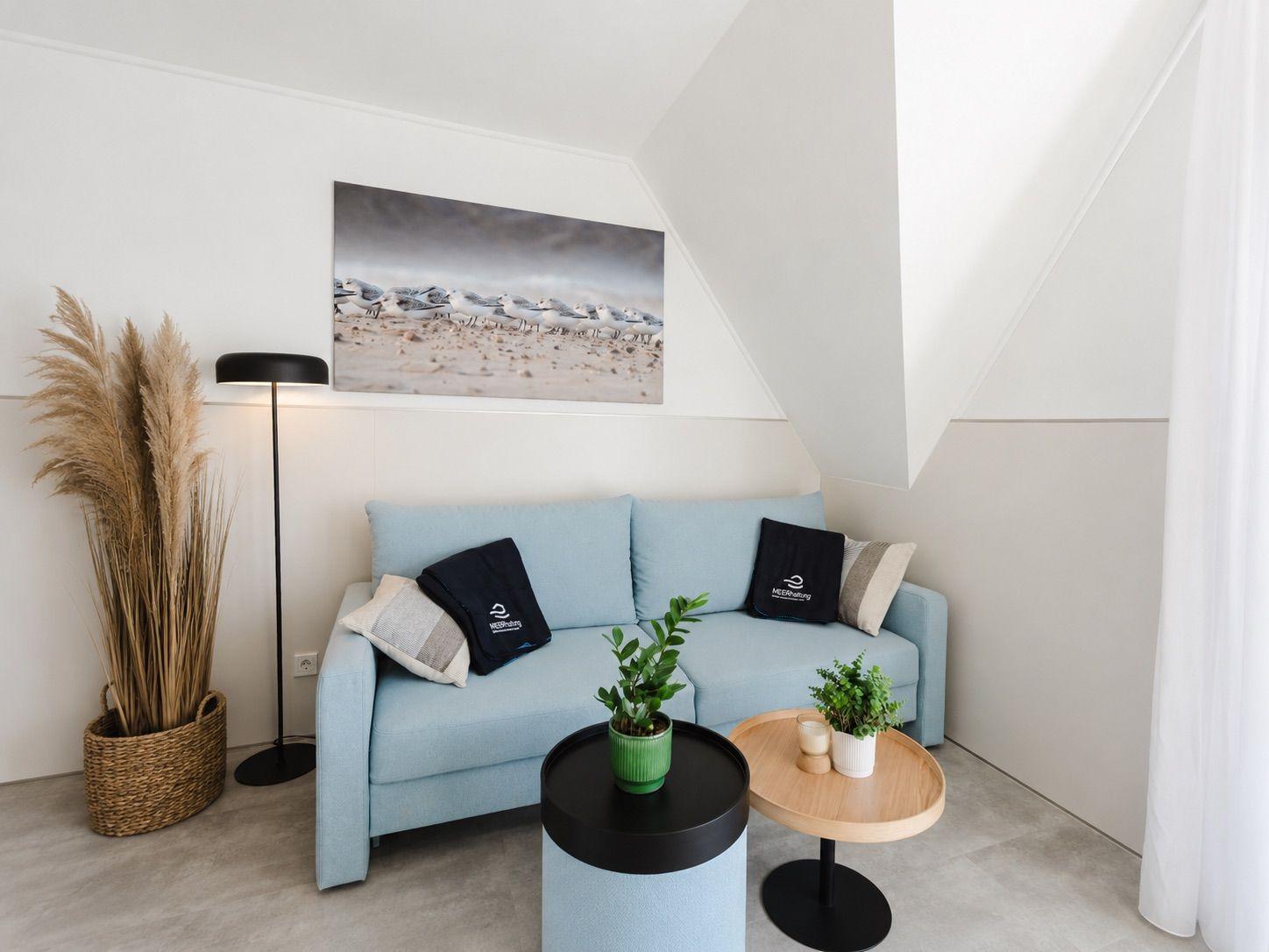 Ein Wohnbereich mit einem hellblauen Sofa, zwei Tischen und einer Wanddekoration.
