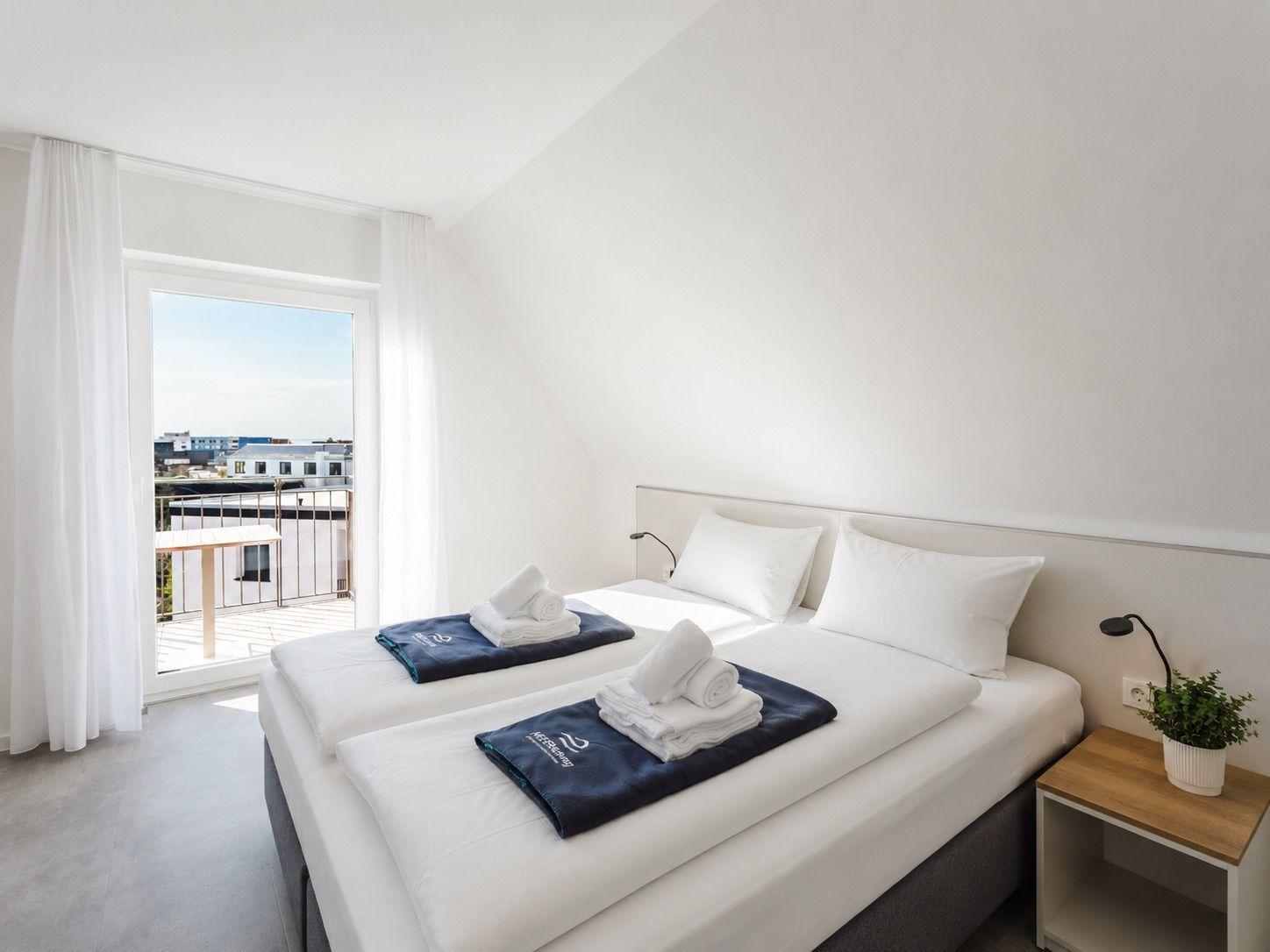 Zimmer mit Doppelbett, Balkon und Nachttisch mit Pflanze.
