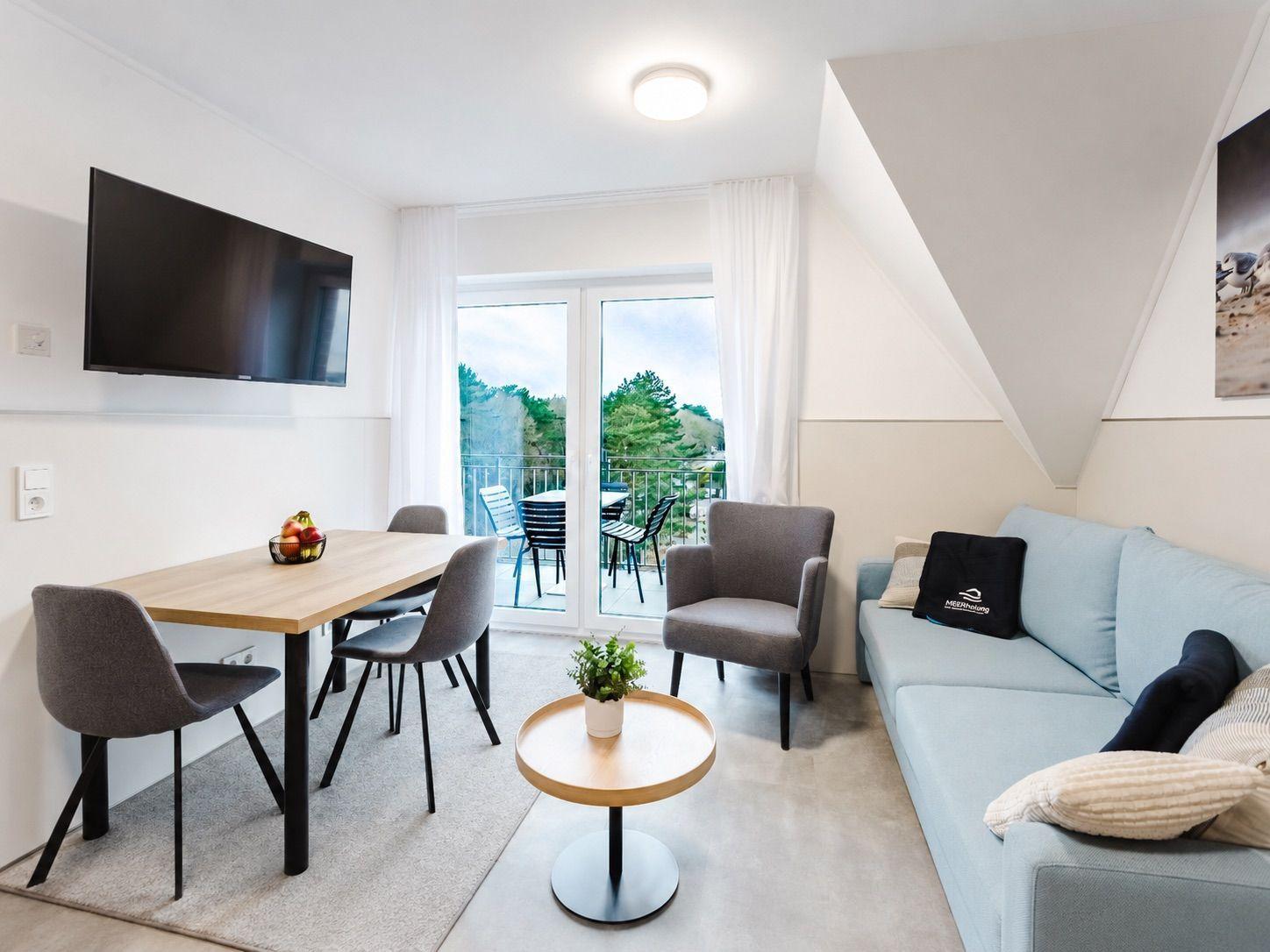 Wohnzimmer mit Esstisch, Sofa und Balkon. Fernseher an der Wand.