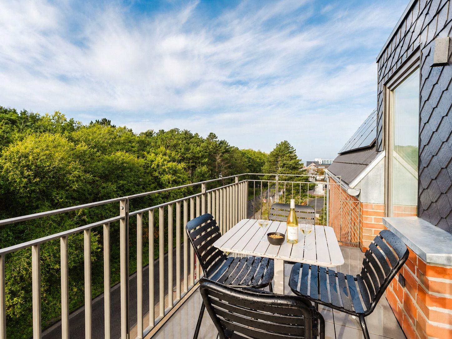 Balcony with table and chairs overlooking green trees and sky.