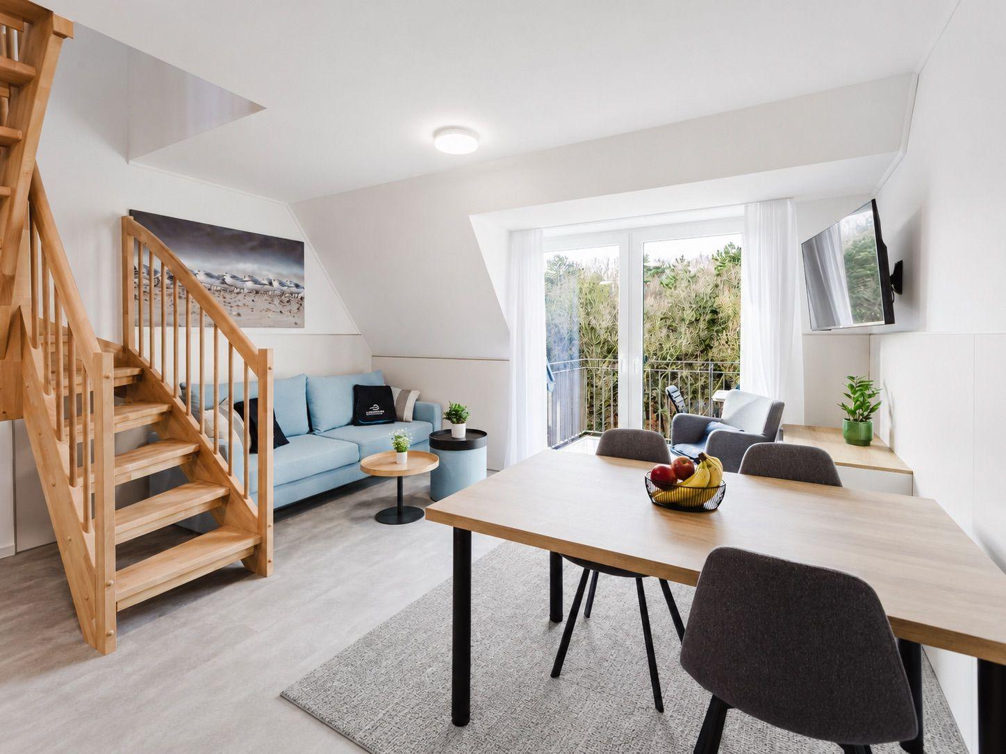 Wohn- und Essbereich mit Holztreppe, Sofa und Balkonansicht.