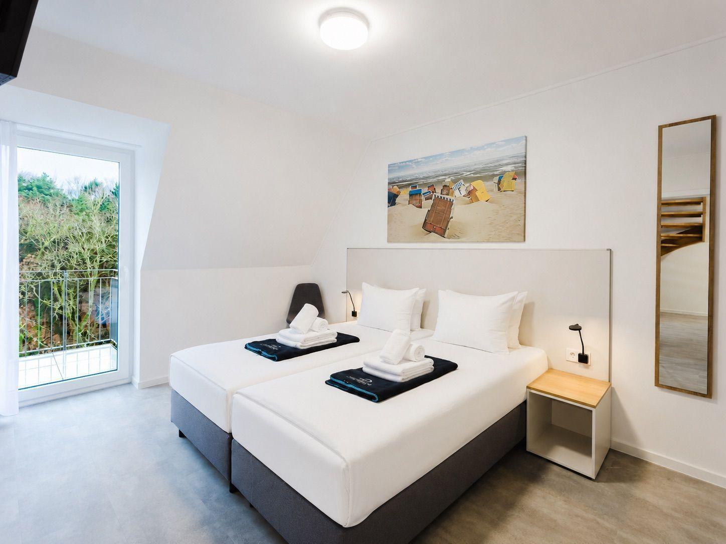 Zimmer mit Doppelbett, Balkon und Wandbild. Nachtschrank und Spiegel an der Wand.