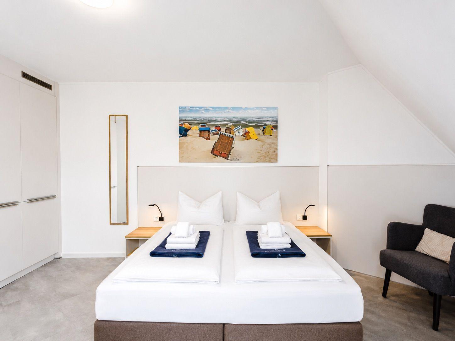 Schlafzimmer mit Doppelbett, Wandbild und Sitzgelegenheit.
