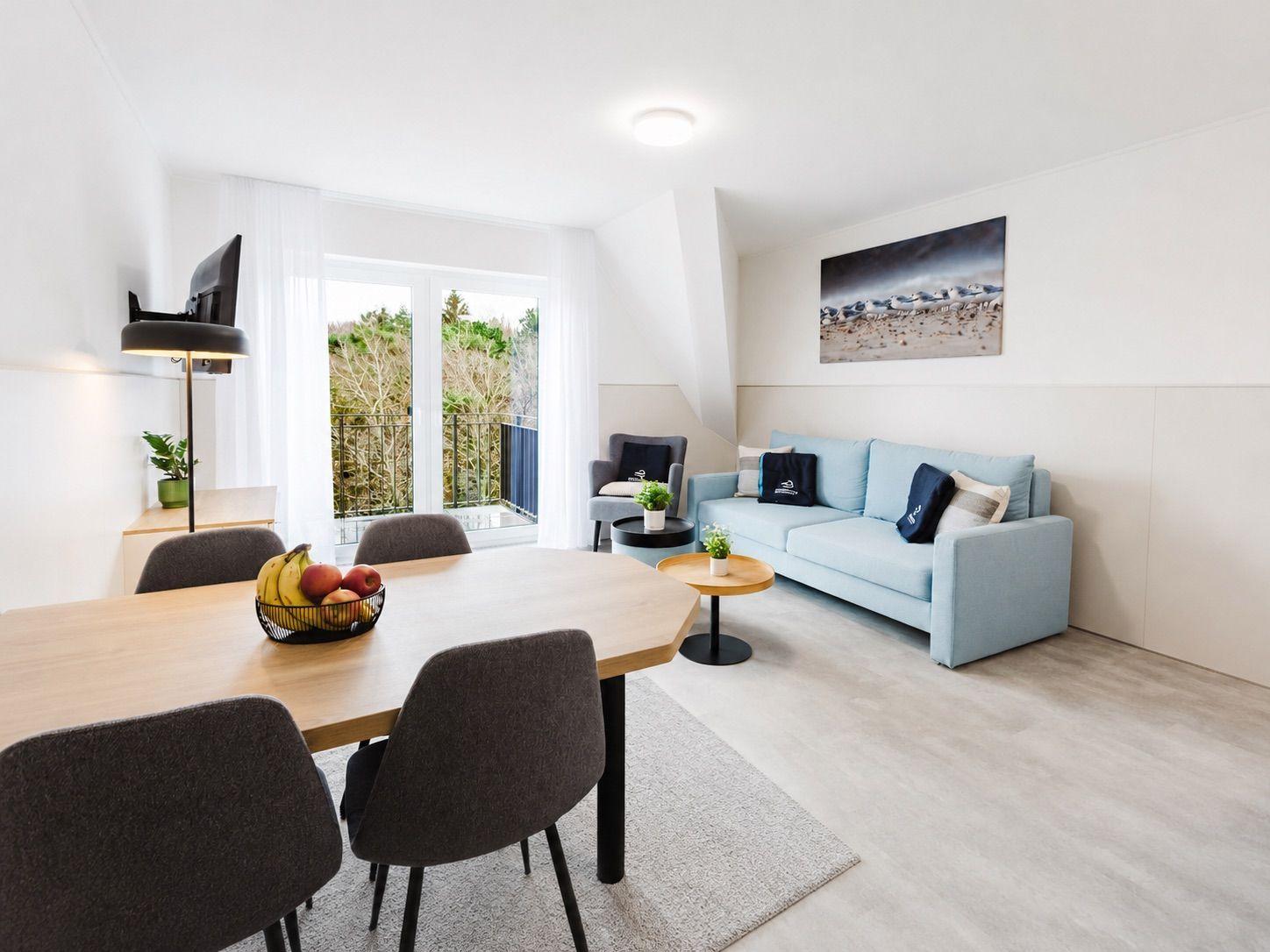 Wohn- und Essbereich mit blauem Sofa, Esstisch und Balkonzugang.