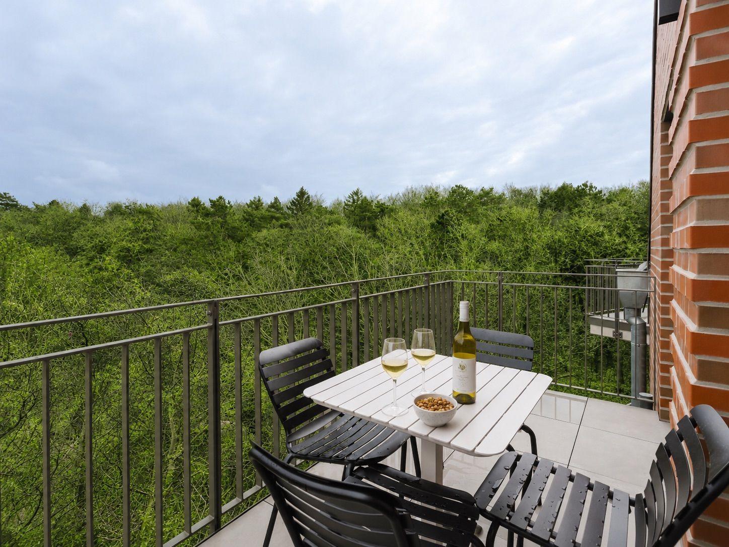 Terrasse mit Tisch, Stühlen, Wein und Nüssen. Blick auf grüne Vegetation.