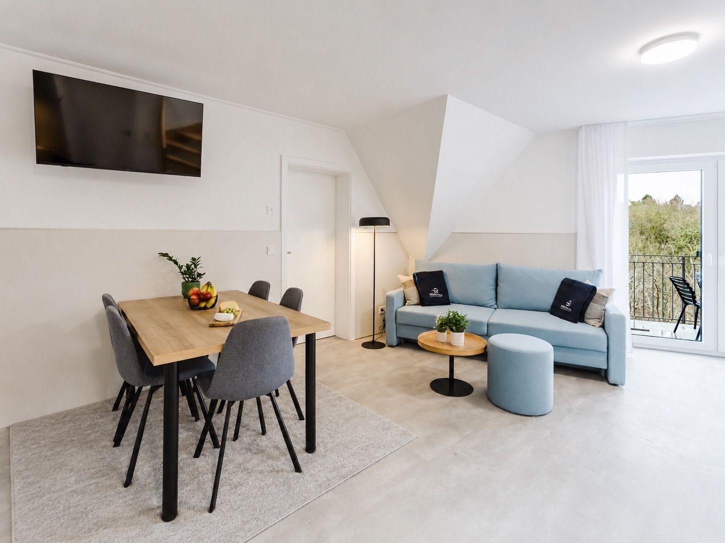 Wohn- und Essbereich mit Sofa, Esstisch und TV. Balkon mit Sicht auf Grün.