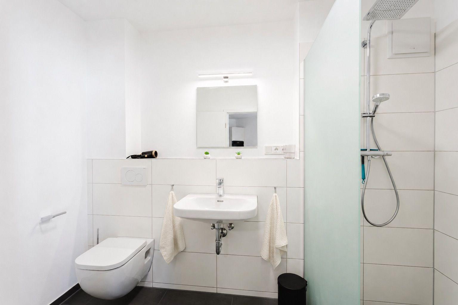 Bathroom with shower, sink, and toilet. White tiles and modern fittings.