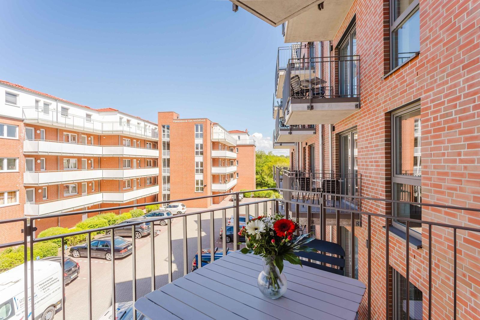 Balcony with table and flowers, view of apartment building and parking lot.