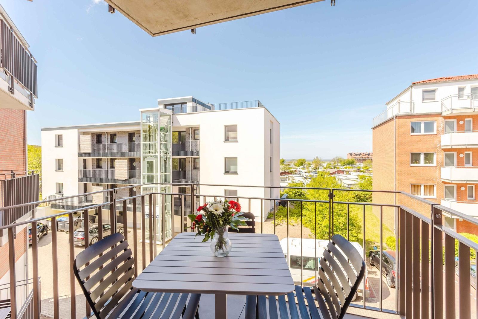 Terrasse mit Tisch und Stühlen, Blick auf Wohnhäuser und Grünflächen.