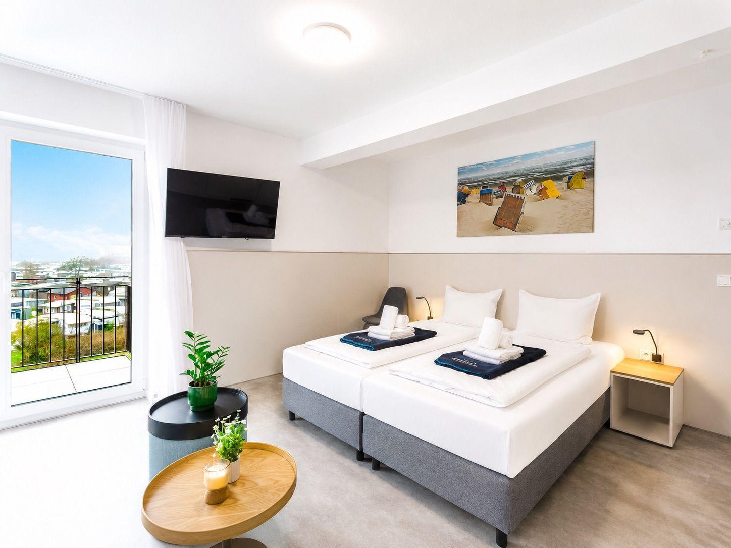 Zimmer mit Doppelbett, Balkon und Wandbild. Fernseher und Nachttische vorhanden.