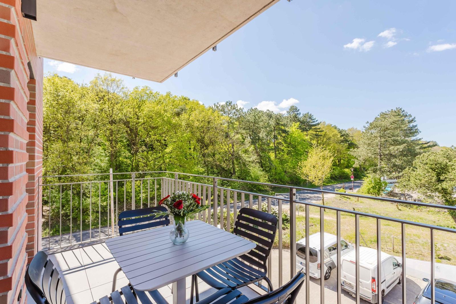Terrasse mit Tisch und Stühlen, Blick auf grüne Bäume und parkende Fahrzeuge.