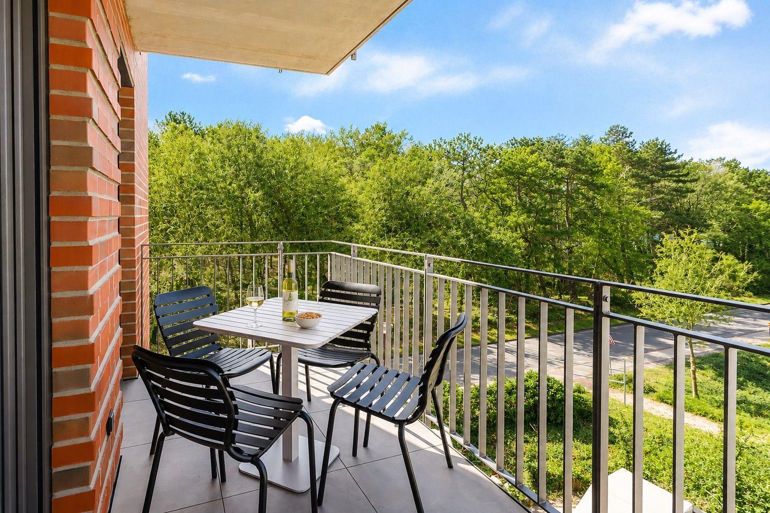 Terrasse mit Tisch und Stühlen, Blick auf grüne Bäume und einen Weg.