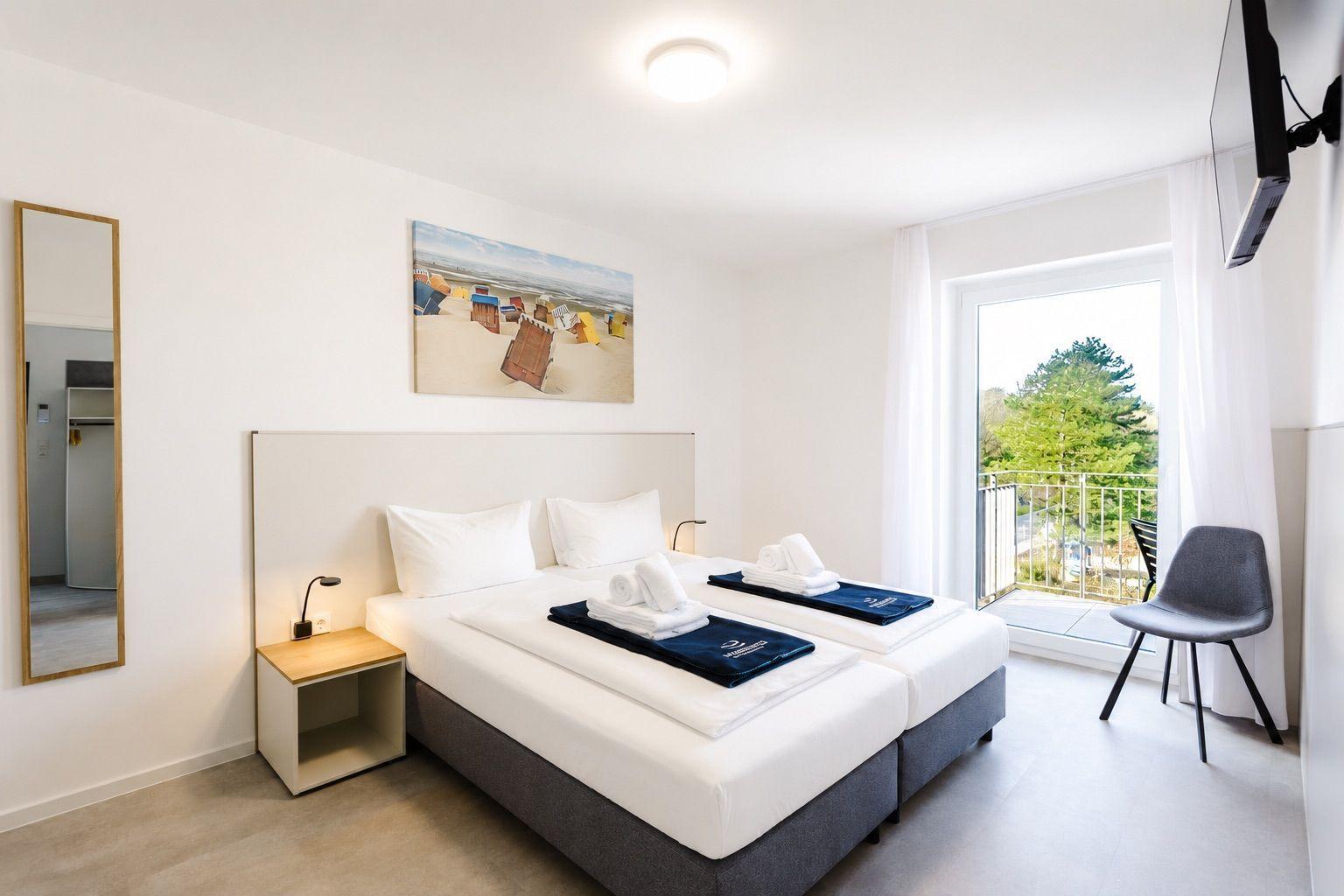 Zimmer mit Doppelbett, Balkon und Wandbild. Helle Wände und moderne Einrichtung.