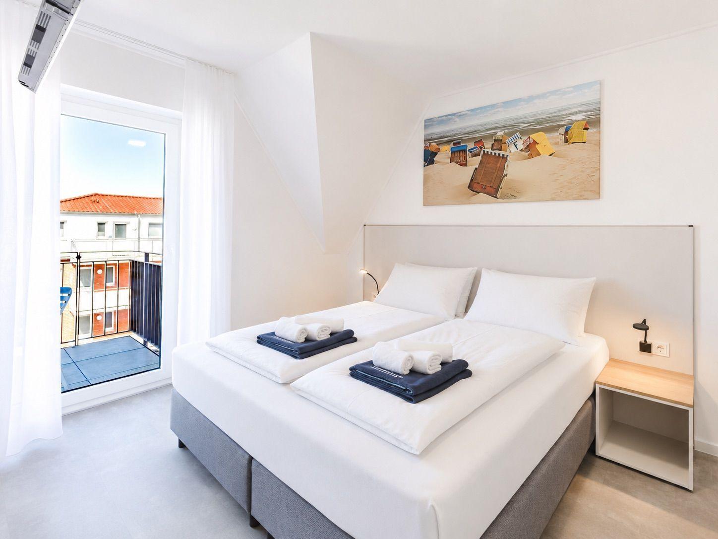 Schlafzimmer mit Doppelbett, Balkon und Strandbild an der Wand.