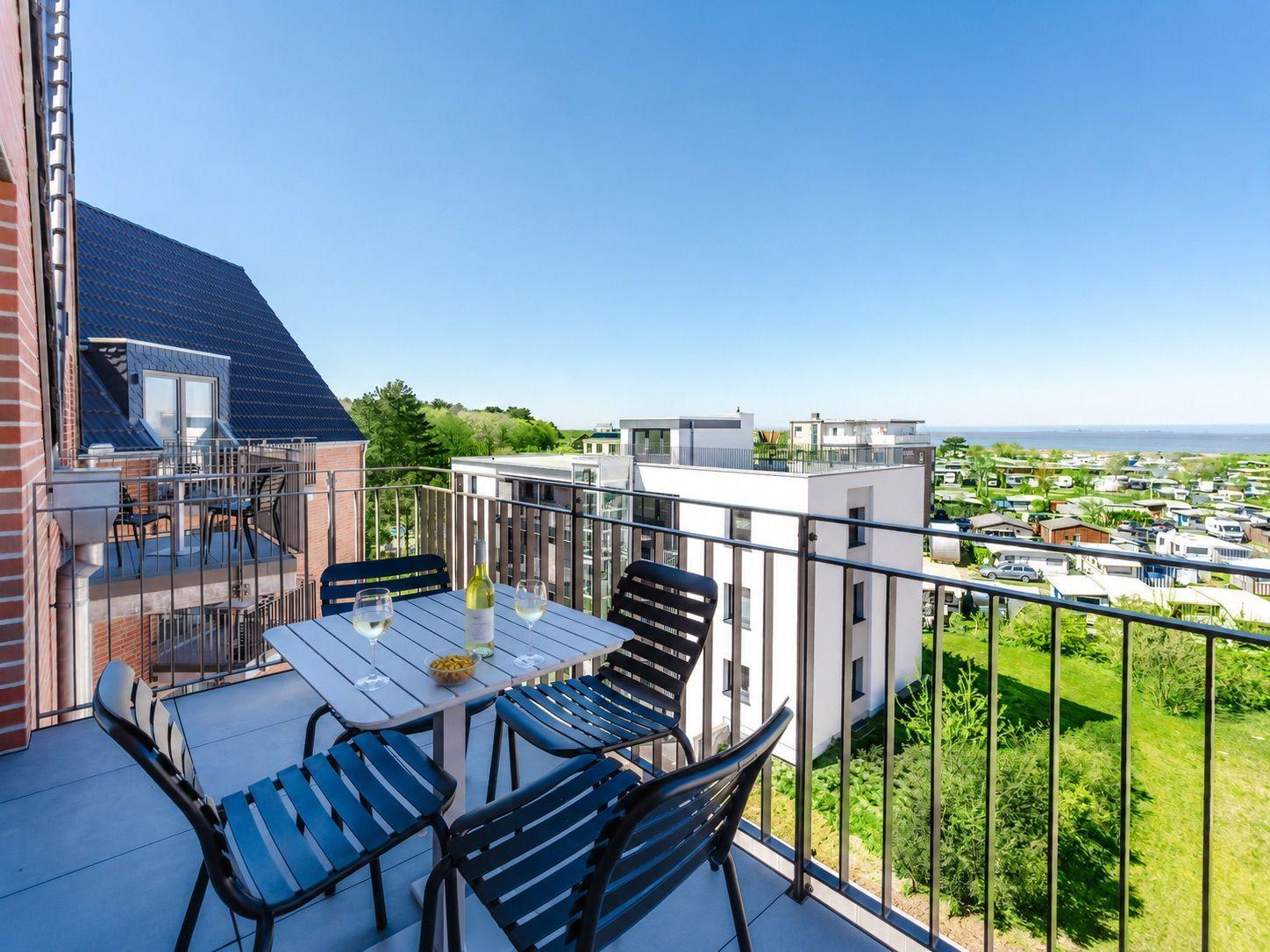 Terrasse mit Tisch und Stühlen, Blick auf Wohngebiet und Meer.
