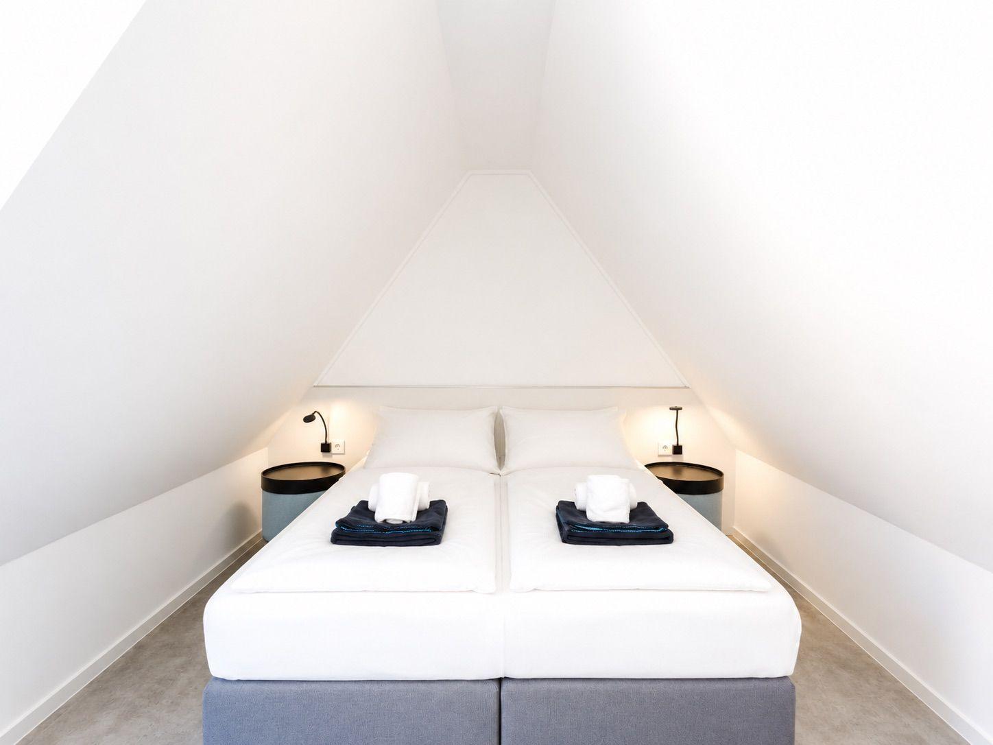 Schlafzimmer mit Doppelbett unter Dachschrägen, zwei Nachttischen und Beleuchtung.