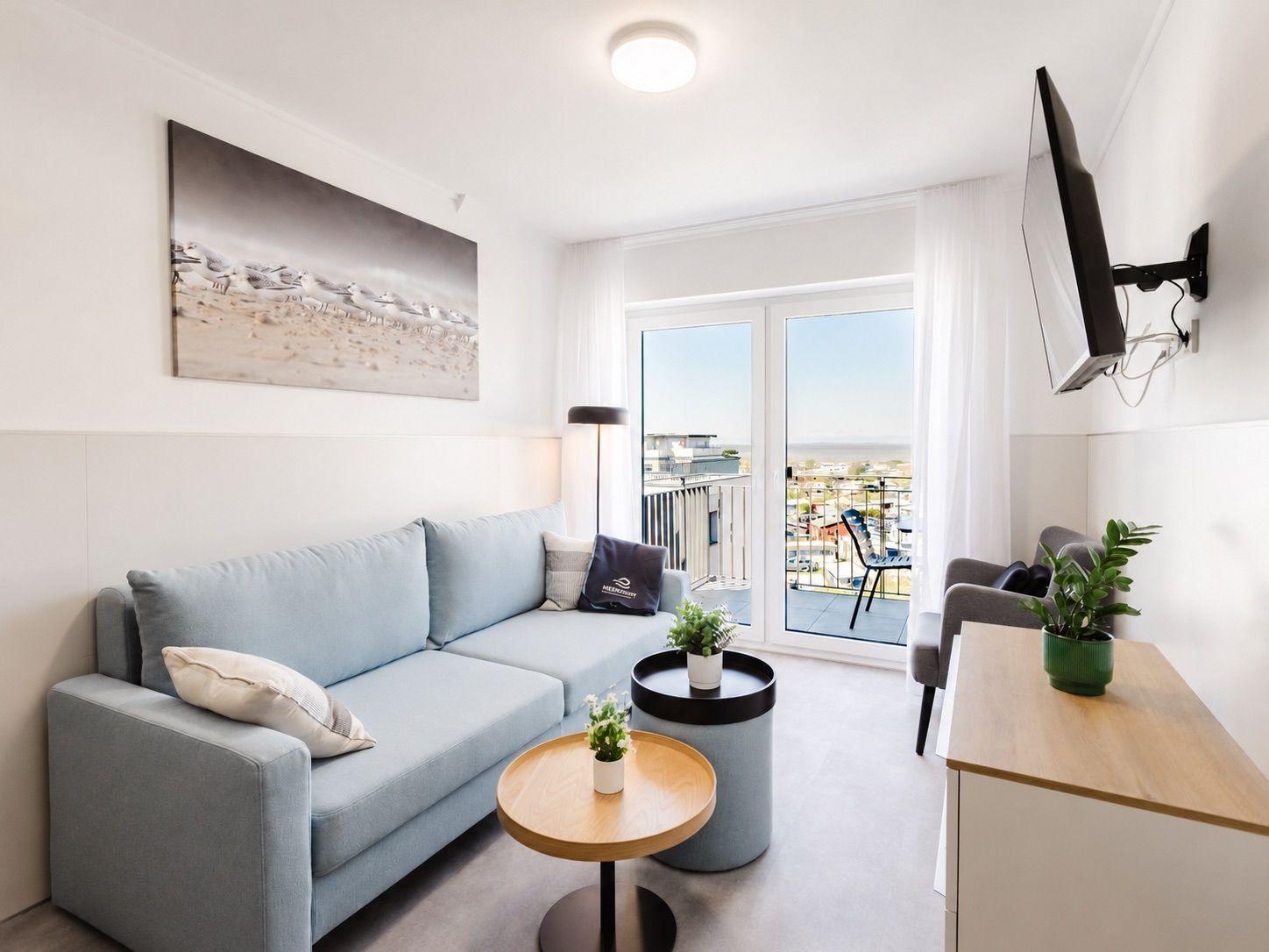 Wohnzimmer mit Sofa, TV und Balkonblick. Holztisch, Pflanzen und Wandbild.