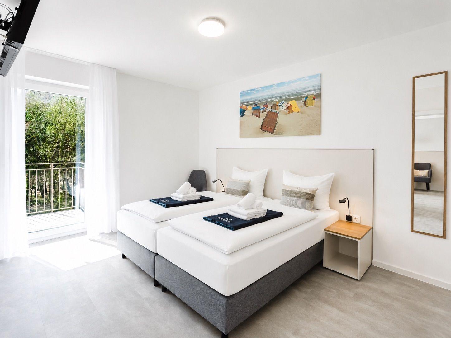 Zimmer mit Doppelbett, Balkon und Wandbild. Nachttisch und Spiegel sind vorhanden.