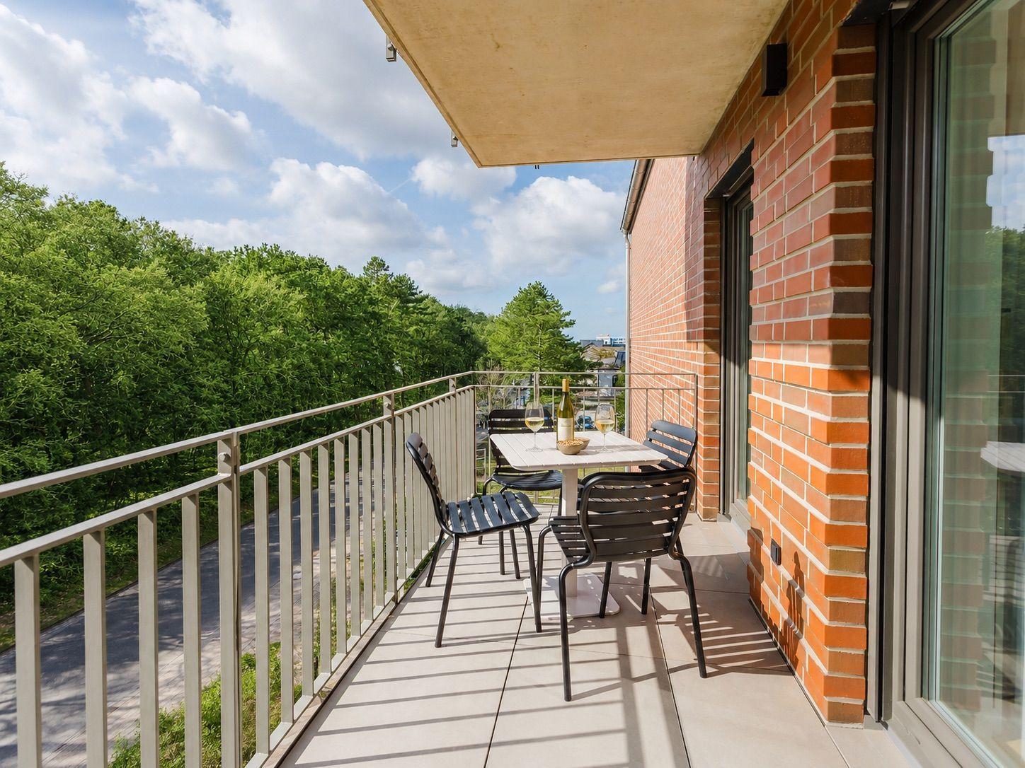 Terrasse mit Tisch und Stühlen, Blick auf grüne Bäume und Himmel.