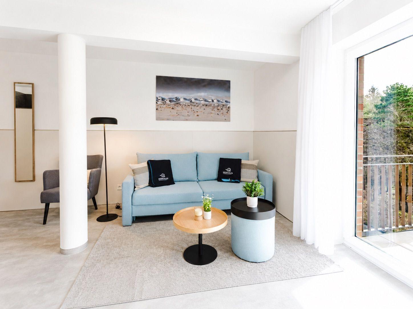 Ein Wohnzimmer mit blauem Sofa, zwei runden Tischen und einer Glastür zum Balkon.
