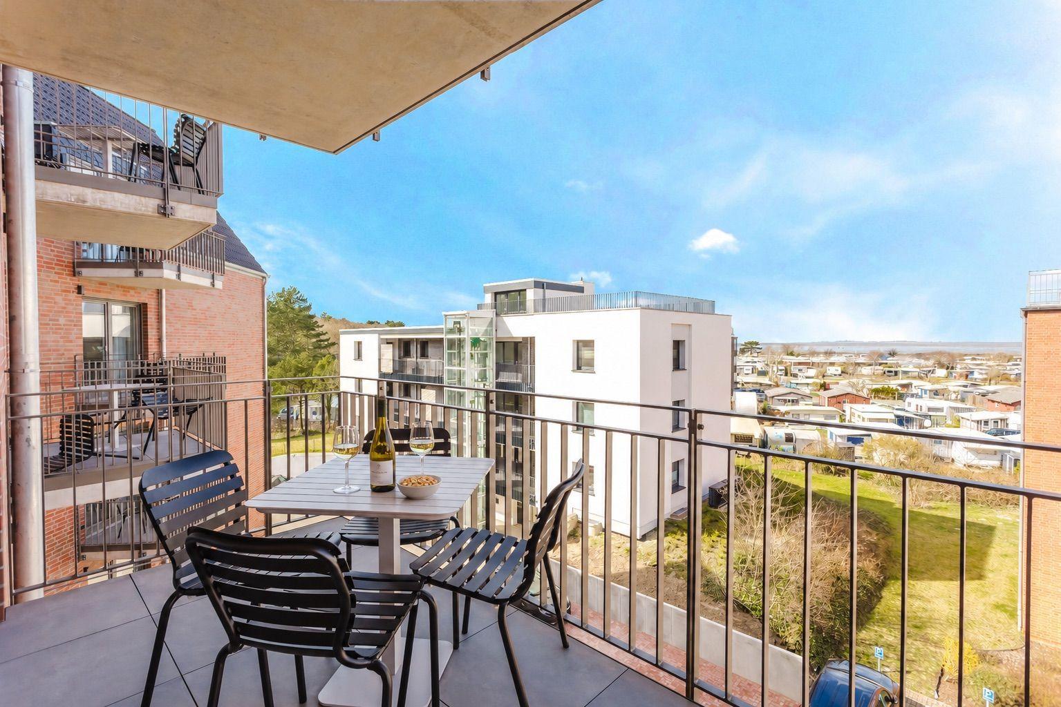 Terrasse mit Tisch und Stühlen, Blick auf moderne Gebäude und Grünflächen.