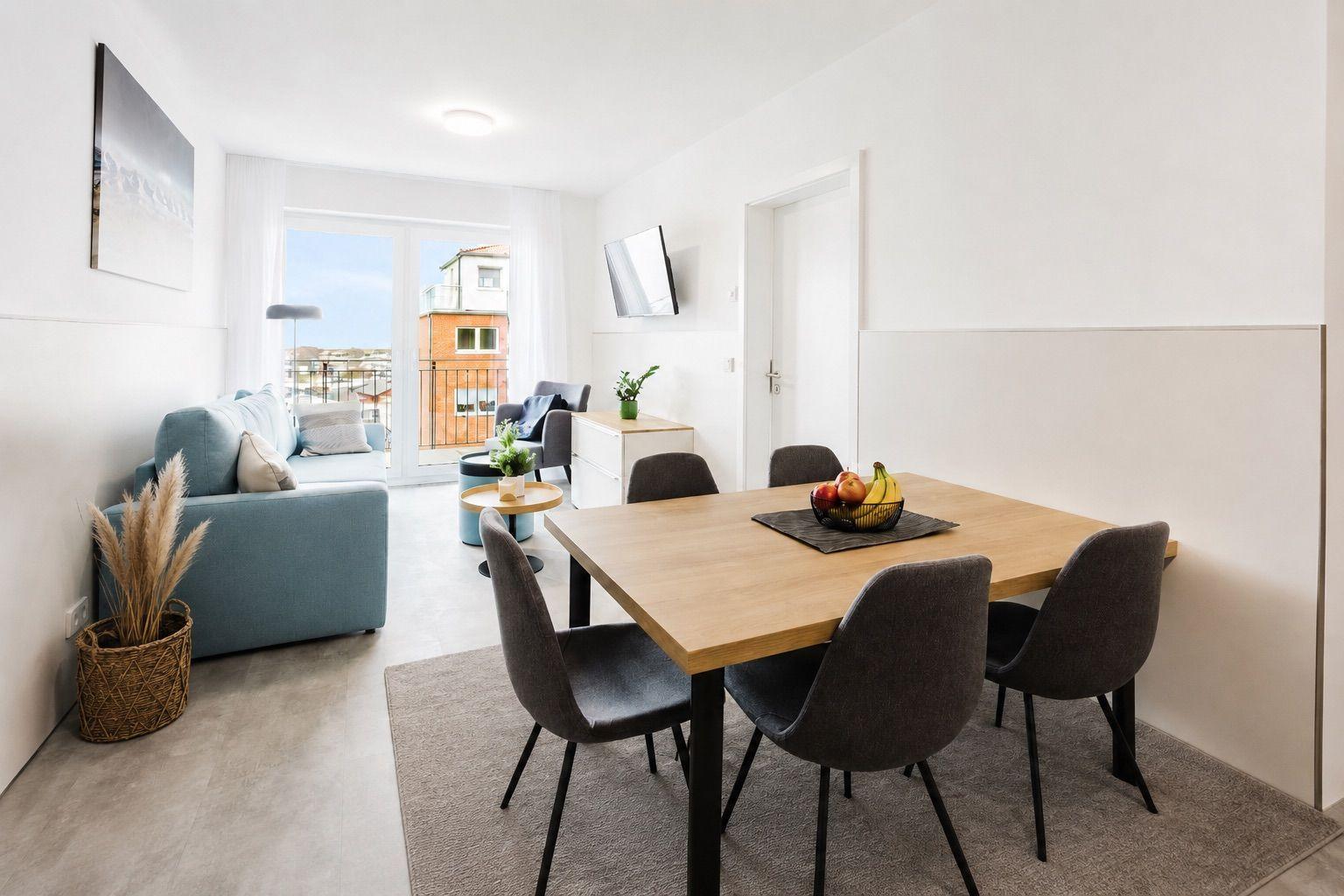 Essbereich mit Tisch und Stühlen, Wohnbereich mit Sofa und Balkontür.