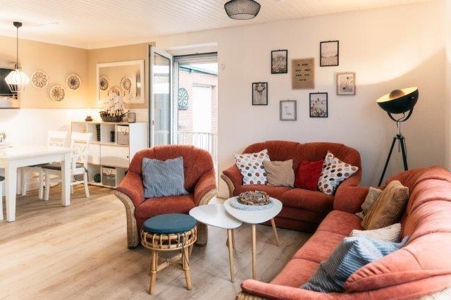Living room with red sofas, table, and chair. Kitchen and balcony in background.