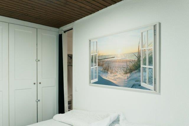 Bedroom with white walls, bed, and large wall pictures with beach motif.