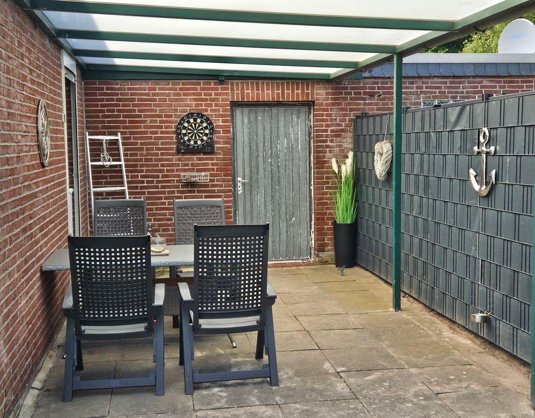 Outdoor area with table, chairs, dartboard, and plant under cover.