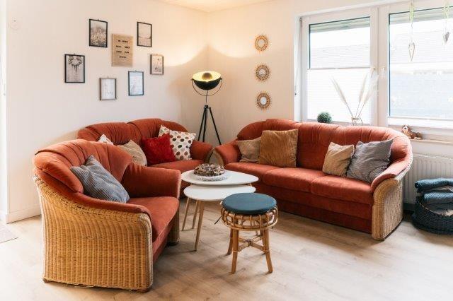 Living room with two orange sofas, table, and stool. Window and wall decor visible.