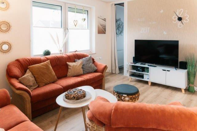Living room with orange sofa, TV, and wooden floor.