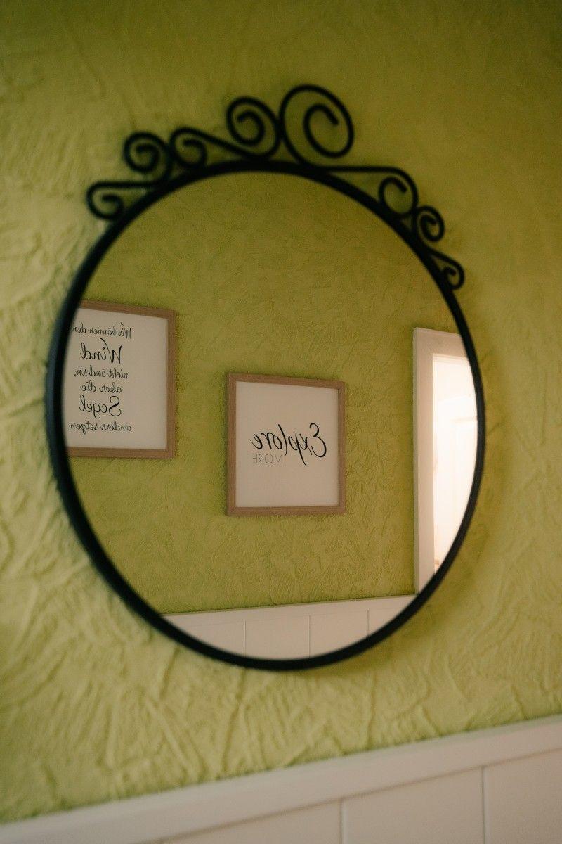 Round mirror with black frame on green wall finish. Two framed pictures are visible.