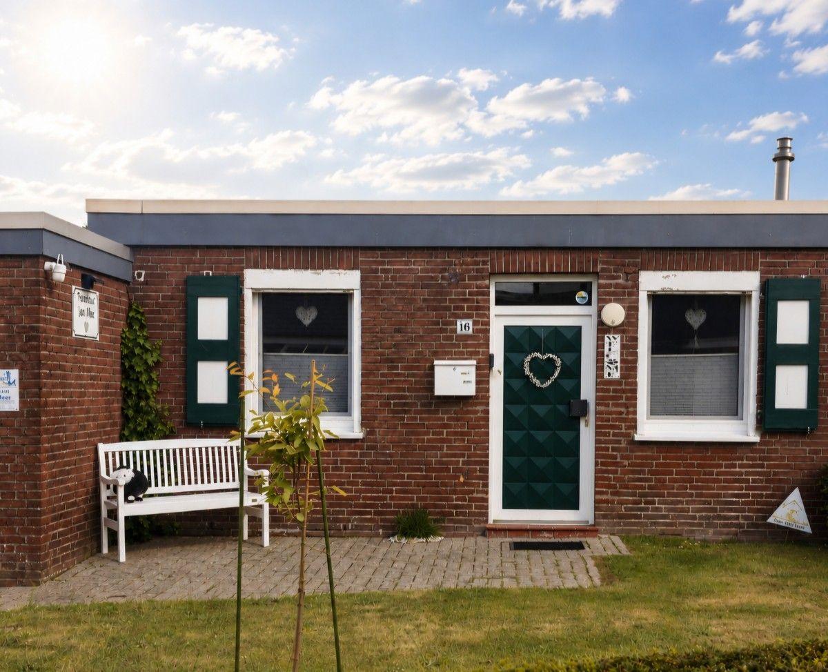A red brick house with a green door and white window frames. A white bench is in front of the entrance.