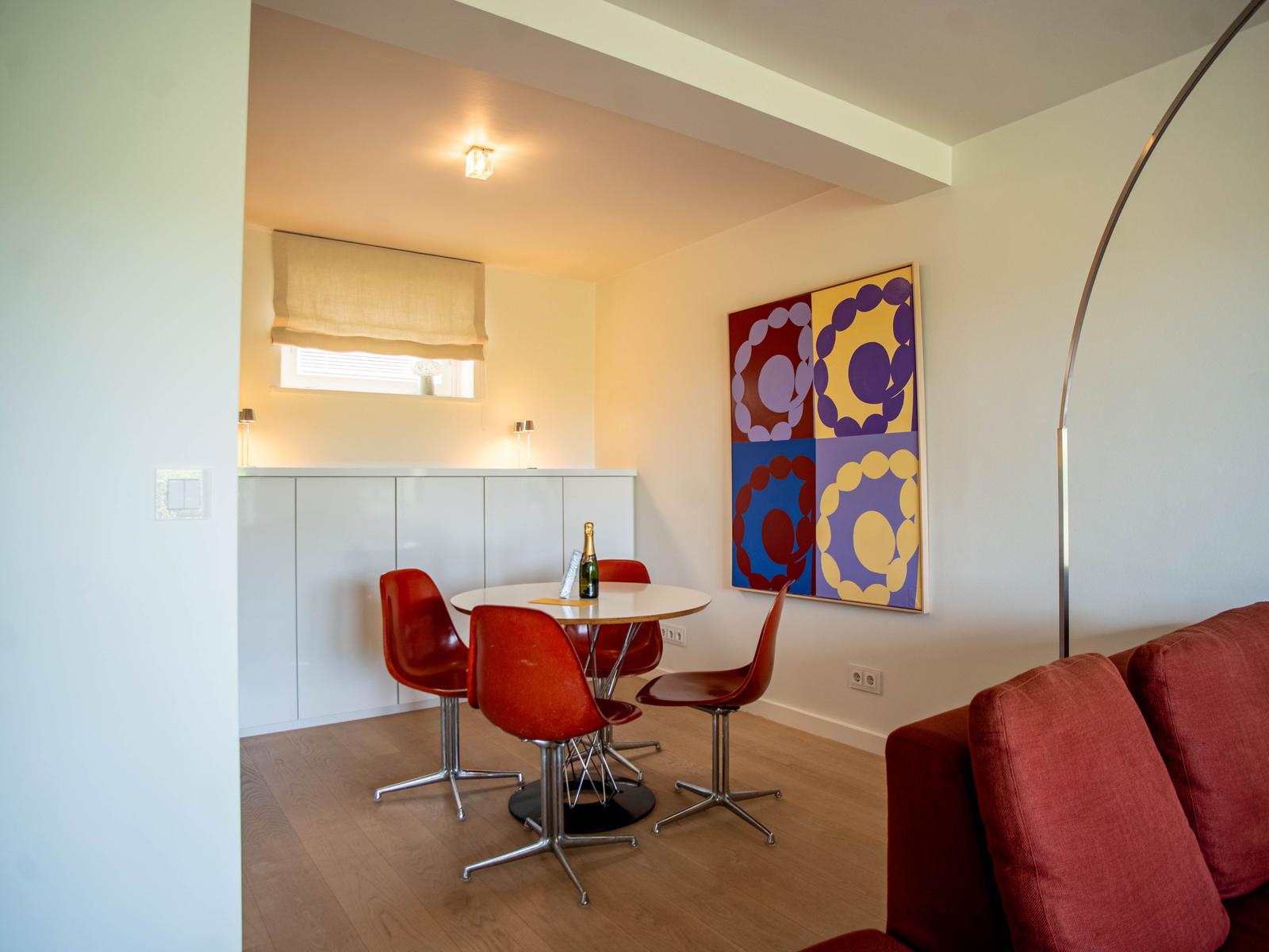 Essbereich mit runden Tisch, roten Stühlen und Wandbild. Sofa und Boden sind rot.