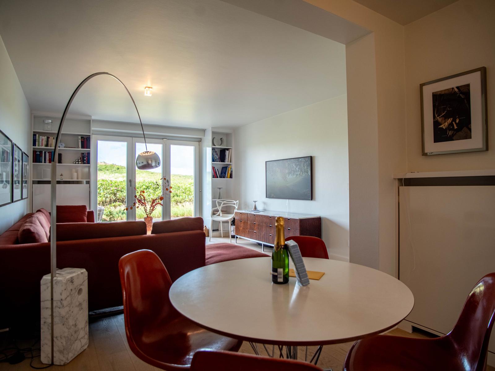 Essbereich mit runden Tisch und roten Stühlen. Wohnbereich mit Sofa und TV.