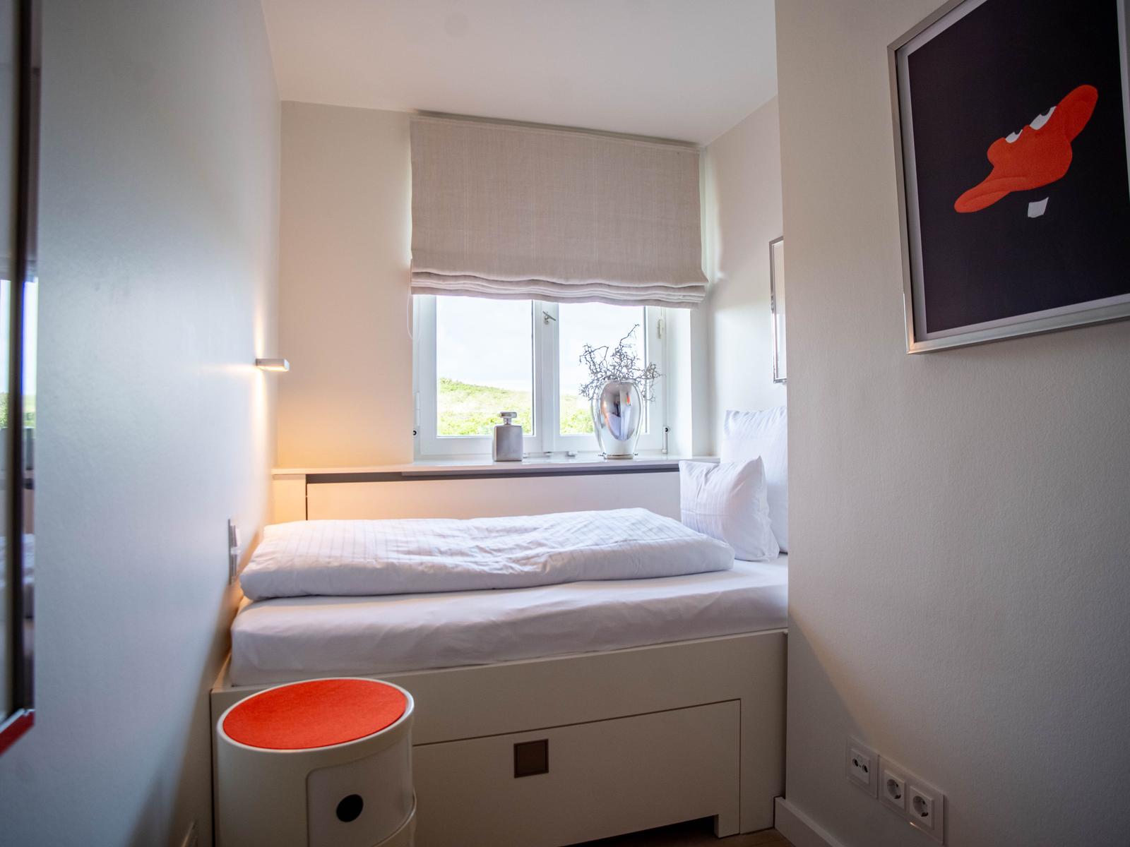 Schlafzimmer mit weißem Bett, Fenster und Kunstwerk an der Wand.