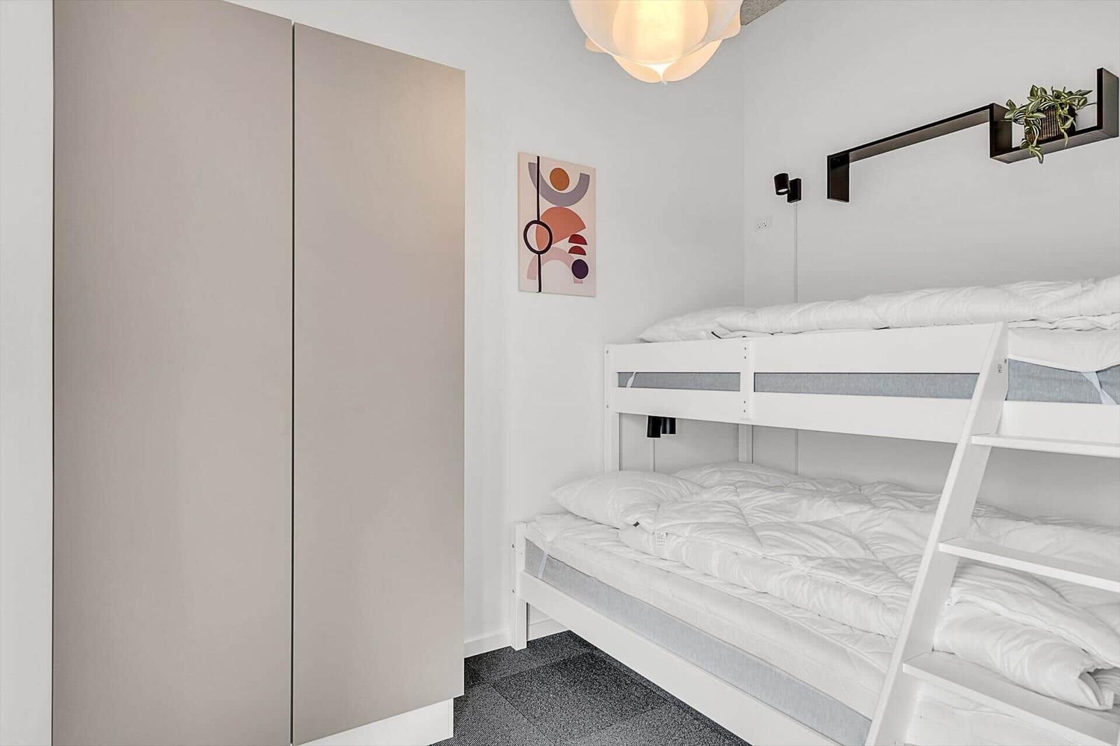 Zimmer mit Doppelstockbett, Kleiderschrank und Wandbild.