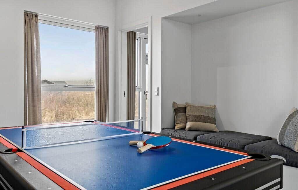 Tischtennis-Tisch mit Schlägern und Ball. Fenster und Sitzgelegenheit im Hintergrund.