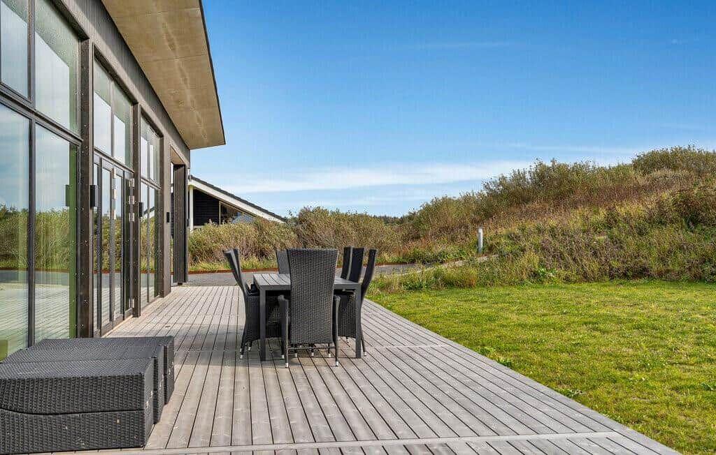 Terrasse mit Tisch und Stühlen neben modernem Haus mit großem Glasbereich.