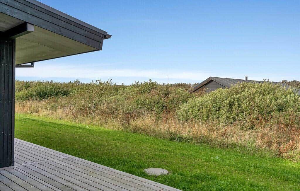 Terrasse mit Blick auf Grasfläche und Büsche. Im Hintergrund ist ein Haus sichtbar.